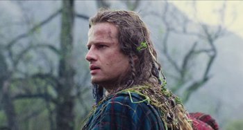 Movie still from “Highlander” (1986), directed by Russell Mulcahy – A man with long blonde hair is wearing a plaid shirt; Close Up shot, Low angle