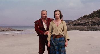 Movie still from “Highlander” (1986), directed by Russell Mulcahy – A man standing next to another man on a beach; Medium shot, Over the shoulder angle