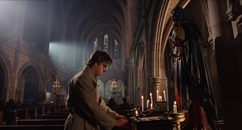 Movie still from “Highlander” (1986), directed by Russell Mulcahy – A man standing in front of candles in a church; Wide shot, Low angle