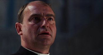 Movie still from “Highlander” (1986), directed by Russell Mulcahy – A person wearing a priest's outfit; Close Up shot, Low angle