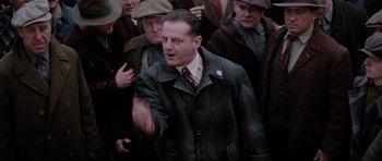 Movie still from “Hoffa” (1992), directed by Danny DeVito – A man in a crowd of people talking to each other; Medium shot, Low angle