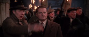 Movie still from “Hoffa” (1992), directed by Danny DeVito – A man wearing a suit and tie standing in front of a group of people; Medium shot, Over the shoulder angle