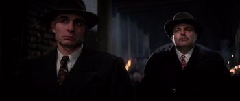 Movie still from “Hoffa” (1992), directed by Danny DeVito – A man in a suit and a hat standing next to another man in a hat; Close Up shot, Low angle
