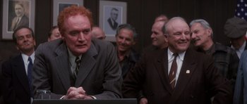 Movie still from “Hoffa” (1992), directed by Danny DeVito – A group of men in suits and ties looking at something; Medium shot, Over the shoulder angle