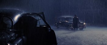 Movie still from “Hoffa” (1992), directed by Danny DeVito – A man standing in the rain next to an old car; Wide shot, High angle