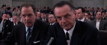Movie still from “Hoffa” (1992), directed by Danny DeVito – A man in a suit and tie sitting next to another man in a suit and tie in front of a crowd; Close Up shot, Low angle