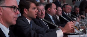 Movie still from “Hoffa” (1992), directed by Danny DeVito – A group of men in suits and ties sitting at microphones in front of microphones; Close Up shot, Over the shoulder angle
