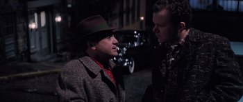 Movie still from “Hoffa” (1992), directed by Danny DeVito – A man wearing a hat is smoking a cigarette while another man is talking to him; Medium shot, Over the shoulder angle