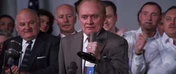 Movie still from “Hoffa” (1992), directed by Danny DeVito – A man in a suit and tie holding a microphone; Close Up shot, Low angle