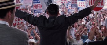 Movie still from “Hoffa” (1992), directed by Danny DeVito – A man with his hands up in front of a crowd of people; Medium shot, Low angle