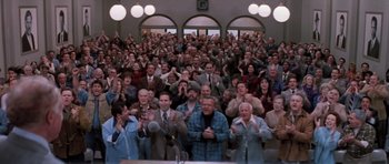 Movie still from “Hoffa” (1992), directed by Danny DeVito – A group of people standing in front of a microphone; Wide shot, High angle