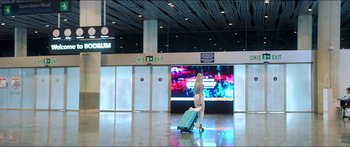 Movie still from “Holiday” (2018), directed by Isabella Eklöf – A woman pulling a suitcase in an airport terminal; Extreme Wide shot, Low angle