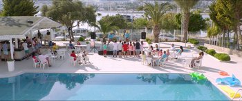 Movie still from “Holiday” (2018), directed by Isabella Eklöf – A group of people sitting around a pool; Extreme Wide shot, High angle