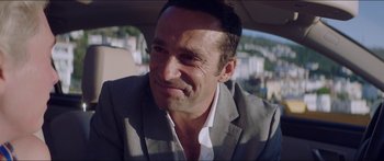 Movie still from “Holiday” (2018), directed by Isabella Eklöf – A person wearing a suit in a car; Close Up shot, Over the shoulder angle