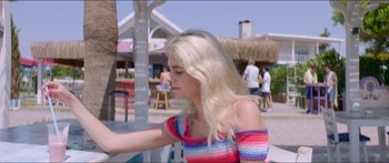 Movie still from “Holiday” (2018), directed by Isabella Eklöf – A woman with long blonde hair sitting at an outdoor table; Medium shot, High angle