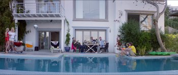 Movie still from “Holiday” (2018), directed by Isabella Eklöf – A group of people sitting at a table near a pool; Wide shot, High angle