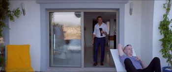 Movie still from “Holiday” (2018), directed by Isabella Eklöf – A man standing in front of an open sliding glass door; Wide shot, Over the shoulder angle