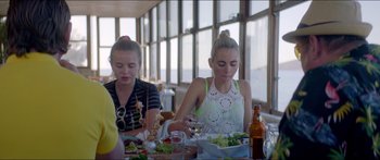Movie still from “Holiday” (2018), directed by Isabella Eklöf – Two young women sitting at a table with a plate of food; Medium shot, Over the shoulder angle