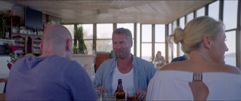 Movie still from “Holiday” (2018), directed by Isabella Eklöf – A man sitting at a table with a bottle of beer; Medium shot, Over the shoulder angle