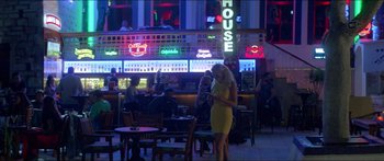 Movie still from “Holiday” (2018), directed by Isabella Eklöf – A woman in a yellow dress standing next to a table; Extreme Wide shot, High angle