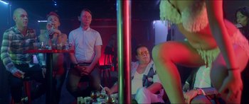 Movie still from “Holiday” (2018), directed by Isabella Eklöf – A group of men sitting around a pole in a room; Medium shot, Over the shoulder angle