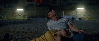 Movie still from “Holiday” (2018), directed by Isabella Eklöf – A man and a woman laying on the ground; Medium shot, High angle