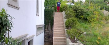 Movie still from “Holiday” (2018), directed by Isabella Eklöf – A man standing on the steps leading up to a house; Extreme Wide shot, Low angle