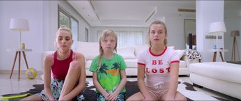 Movie still from “Holiday” (2018), directed by Isabella Eklöf – Three young girls sitting on the ground in front of a couch; Medium shot, High angle