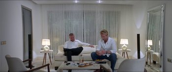 Movie still from “Holiday” (2018), directed by Isabella Eklöf – Two men sitting on a couch in a living room; Wide shot, High angle
