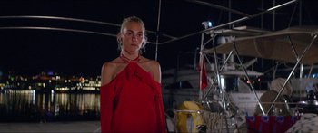 Movie still from “Holiday” (2018), directed by Isabella Eklöf – A woman in a red dress standing in front of a boat at night; Medium shot, Low angle