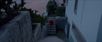 Movie still from “Holiday” (2018), directed by Isabella Eklöf – A woman walking up a set of stairs near a body of water; Extreme Wide shot, Overhead angle