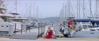 Movie still from “Holiday” (2018), directed by Isabella Eklöf – A woman in a red dress sitting on the ground near boats; Extreme Wide shot, High angle