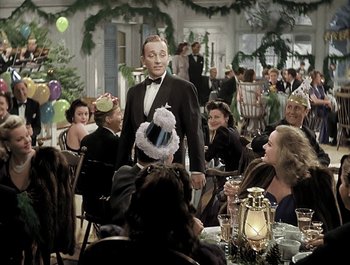 Movie still from “Holiday Inn” (1942), directed by Robert Allen – A group of people sitting at a table with a man in a tuxedo; Medium shot, High angle