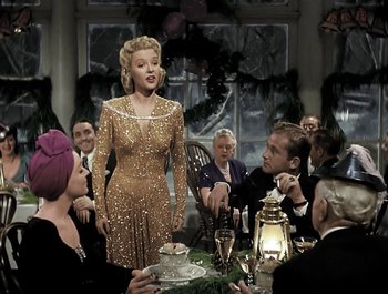 Movie still from “Holiday Inn” (1942), directed by Robert Allen – A group of people sitting around a table with a woman in a gold dress; Medium shot, High angle