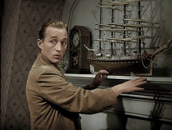 Movie still from “Holiday Inn” (1942), directed by Robert Allen – A man holding out his hand in front of a model ship; Medium shot, High angle