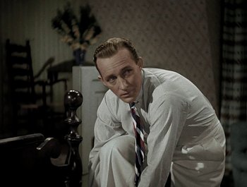 Movie still from “Holiday Inn” (1942), directed by Robert Allen – A man in a white shirt and tie leaning against a wooden post; Medium shot, High angle