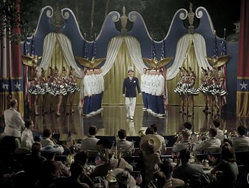 Movie still from “Holiday Inn” (1942), directed by Robert Allen – A group of people are standing in front of a stage; Extreme Wide shot, High angle