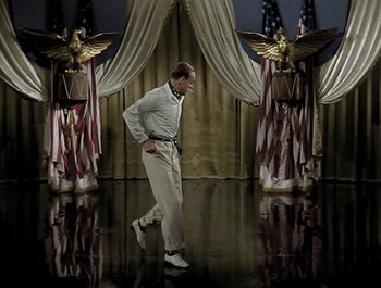 Movie still from “Holiday Inn” (1942), directed by Robert Allen – A man walking in front of american flags and curtains; Wide shot, High angle