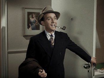 Movie still from “Holiday Inn” (1942), directed by Robert Allen – A man wearing a suit and hat smoking a pipe; Medium shot, High angle