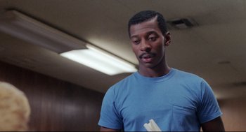 Movie still from “Hollywood Shuffle” (1987), directed by Robert Townsend – A man in a blue t - shirt is holding something in his hand; Close Up shot, Low angle