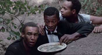 Movie still from “Hollywood Shuffle” (1987), directed by Robert Townsend – A group of men sitting next to each other on the ground; Medium shot, High angle