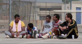 Movie still from “Hollywood Shuffle” (1987), directed by Robert Townsend – A group of young men sitting on the ground next to each other; Wide shot, Low angle