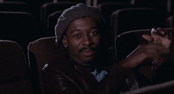 Movie still from “Hollywood Shuffle” (1987), directed by Robert Townsend – A man sitting in a chair wearing a hat; Close Up shot, Low angle