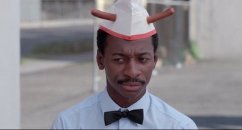 Movie still from “Hollywood Shuffle” (1987), directed by Robert Townsend – A man wearing a paper hat and a bow tie; Close Up shot, Over the shoulder angle
