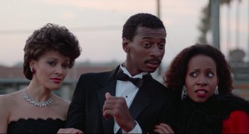 Movie still from “Hollywood Shuffle” (1987), directed by Robert Townsend – Two women and a man in a tuxedo posing for a picture; Close Up shot, Low angle
