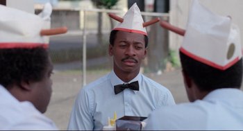 Movie still from “Hollywood Shuffle” (1987), directed by Robert Townsend – A man wearing a paper hat and a bow tie; Close Up shot, Over the shoulder angle