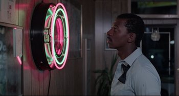 Movie still from “Hollywood Shuffle” (1987), directed by Robert Townsend – A man standing in front of a neon sign; Medium shot, Over the shoulder angle