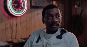 Movie still from “Hollywood Shuffle” (1987), directed by Robert Townsend – A man sitting in front of a neon sign in a restaurant; Close Up shot, Low angle