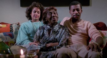 Movie still from “Hollywood Shuffle” (1987), directed by Robert Townsend – A group of three people sitting on a couch together; Medium shot, Low angle