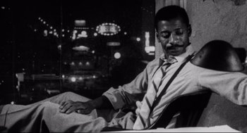 Movie still from “Hollywood Shuffle” (1987), directed by Robert Townsend – A black and white photo of a man sitting on a couch; Medium shot, High angle